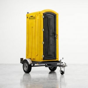 Baño químico amarillo montado sobre carro de arrastre para rápida instalación en terrenos rurales.